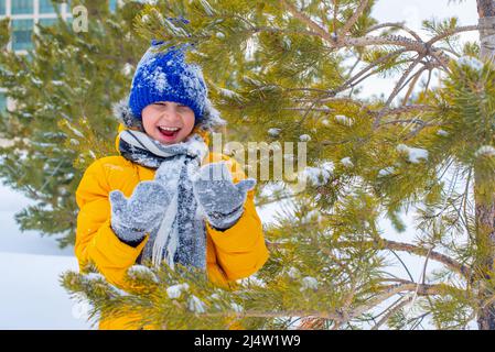 in a blue hat and a yellow jacket a cheerful boy in the snow Stock Photo