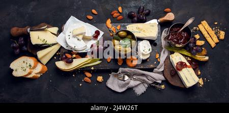 Cheese board on dark background. Celebration gathering. Food for wine, snacks, delicatessen. panorama, flat lay Stock Photo