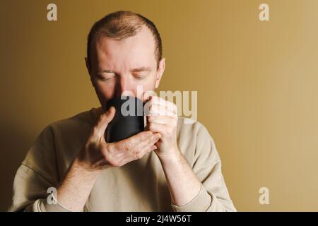 Portrait of a man drinking from a black cup. White unshaven man drinking from a cup Stock Photo