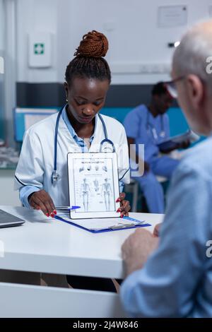 Clinic medic specialist showing diagram of human body to senior patient. Doctor explaining retired man symptoms of curable disease and treatment schedule for health recovery. Stock Photo