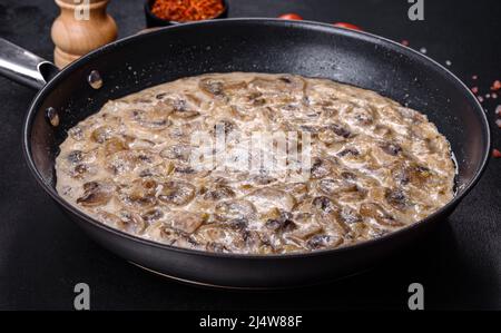 Delicious fresh young champignons sliced into slices in creamy sauce simmered in a black pan Stock Photo