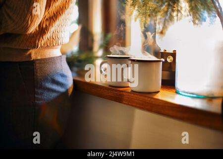 Christmas hot drink - two mugs of mulled red wine with spices and fruits or ot tea on windowsill. New Year decoration on a wooden retro background. Stock Photo