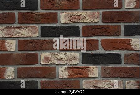 Clinker bricks background. A close-up of a clinker brick wall from dark red, white, orange and black bricks. Stock Photo