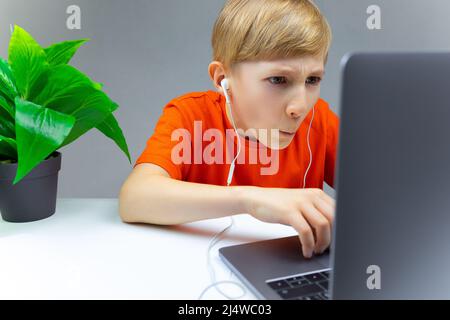 the child works hard at the laptop typing on it and listen to music on headphones Stock Photo