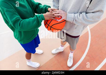 unrecognizable caucasian man and latin woman joining hands over a basketball, concept of friendship and urban sport in the street, copy space for text Stock Photo