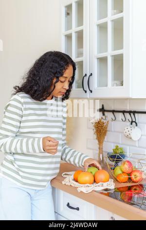 African-American taking out apples and oranges after going at grocery store with eco-bag Stock Photo