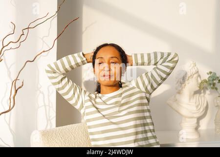 Smiling African-American female looking at window. Natural light from sunset. Enjoying moment Stock Photo