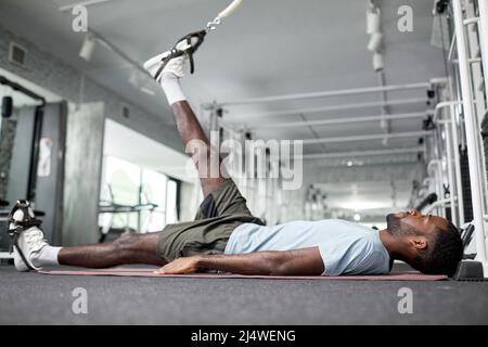 Side view portrait of African American young man doing rehabilitation exercises for leg muscles in gym at physiotherapy clinic Stock Photo