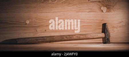 An old hammer with a long handle. Small working tools of a carpenter on a dusty table. Stock Photo