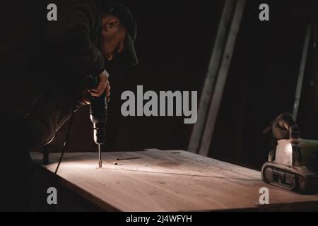 The carpenter works with a hand drill. man drilling a board Stock Photo
