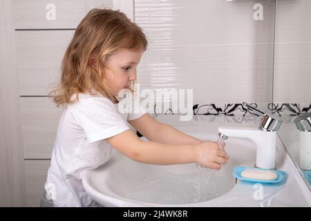 A little girl washes her hands with soap under the tap Stock Photo