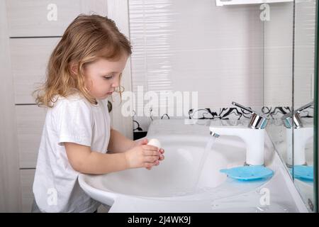 A little girl washes her hands with soap under the tap Stock Photo