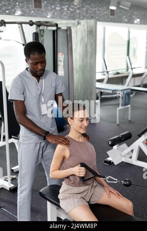Vertical portrait of African American therapist assisting young woman in rehabilitation clinic Stock Photo