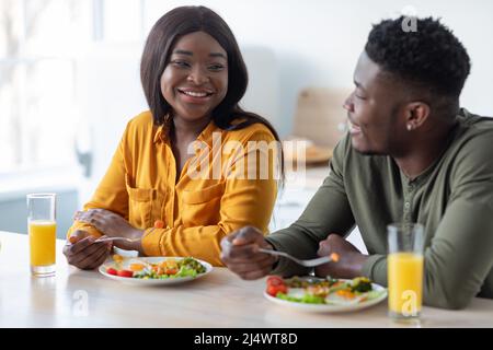 Romantic black spouses having meal together while sitting at table in kitchen Stock Photo