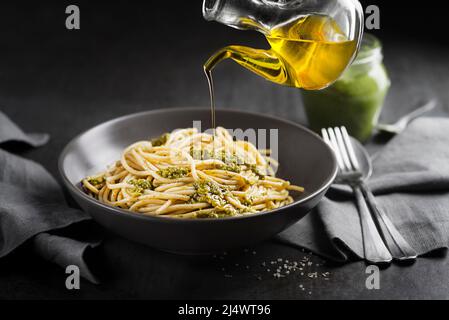 Served spaghetti with fresh basil pesto and pouring with olive oil bottle closeup