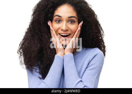 Incredible promotion. Amazed African-American woman in violet color sweater holding cheeks and looks at the camera with mouth open isolated on white, close-up portrait of surprised multiracial lady Stock Photo