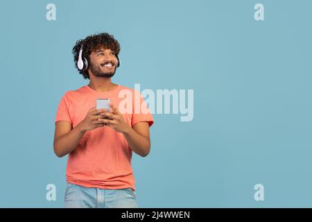 Happy eastern guy using wireless headset and smartphone, copy space Stock Photo