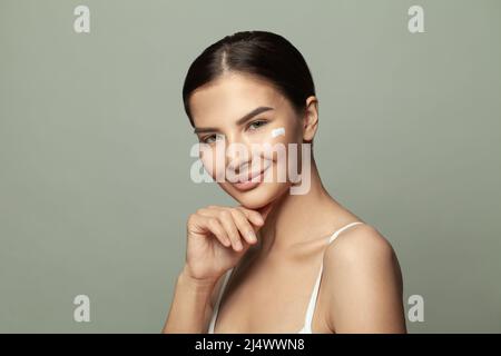 Cheerful beautiful woman applies cream on her face, beauty treatments cares about skin Stock Photo