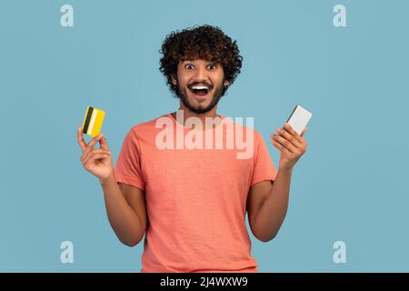Excited hindu guy holding smartphone and credit card Stock Photo
