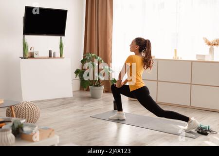 Woman Exercising Doing Standing Lunge Stretch Watching TV At Home Stock Photo