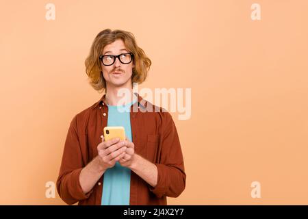 Portrait of attractive minded guy using device choosing copy space smm post isolated over beige pastel color background Stock Photo