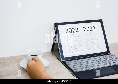 Hand holding coffee cup while looking calendar on digital tablet. Stock Photo