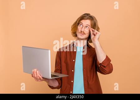 Portrait of handsome minded trendy red-haired guy using laptop deciding isolated over beige pastel color background Stock Photo