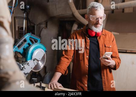 bearded furniture designer using mobile phone near miter saw Stock Photo