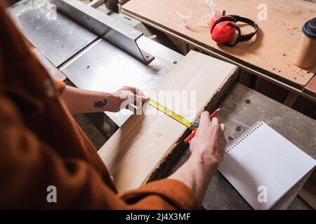 cropped view of furniture designer measuring wooden plank near blank notebook Stock Photo