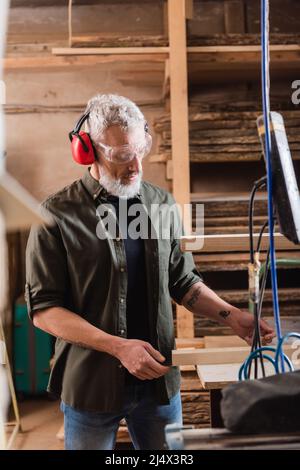 mature woodworker looking at wooden plank in workshop Stock Photo