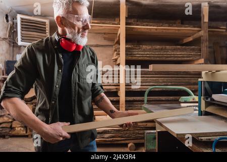 carpenter in goggles holding board near thickness planer Stock Photo