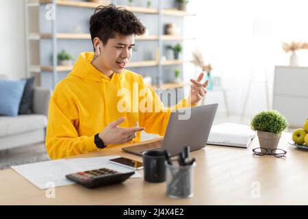 Asian man using laptop wearing headphones sitting at desk Stock Photo