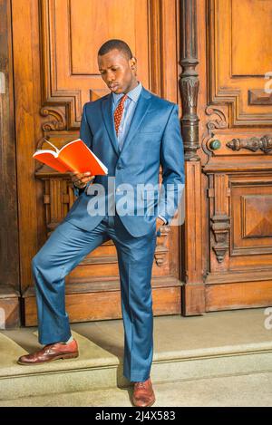 Dressing formally in blue suit, patterned shirt, necktie, short haircut, wearing ear stud, a young black teacher is standing in the front of old style Stock Photo