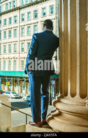 Silhouette of businessman on the phone. Facing street, lowering his head, a young black guy standing by column outside office, talking on his mobile p Stock Photo