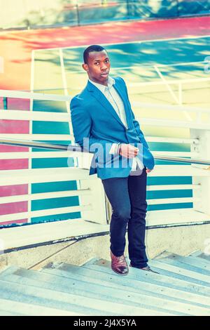 Man Waiting for You. Wearing a blue blazer, black pants,, short haircut, a  young black guy is standing against metal fences by a tennis court, staring  Stock Photo - Alamy