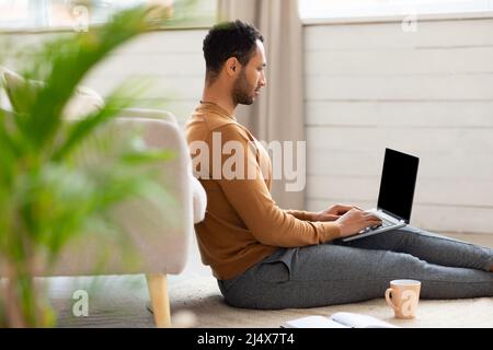 Arab man using laptop sitting on floor at home Stock Photo