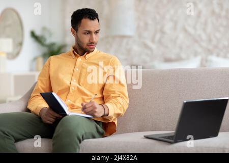 Portrait of focused Arab man using laptop and writing Stock Photo