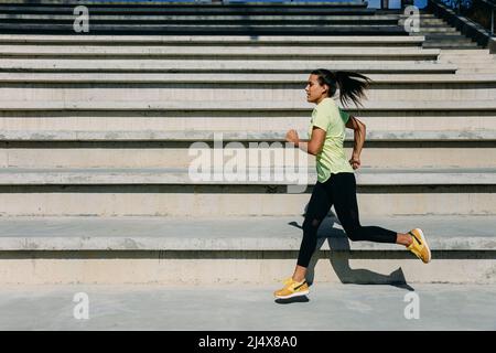 Focused female athlete jumping and running outdoors Stock Photo