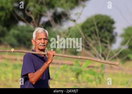 Close-up portrait Photo of A Aged man senior farmer looks at the camera with a wooden stick in his hand Stock Photo