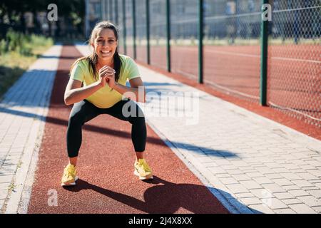 Smiling woman doing squats at local stadium Stock Photo