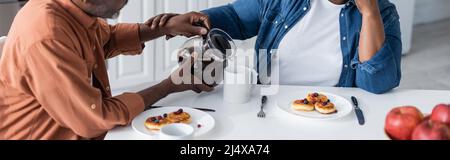 cropped view of senior african american man pouring coffee to wife during breakfast, banner Stock Photo