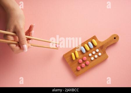 Creative concept flat lay photo with variety of nutritional supplement vitamins and pills arranged as sushi plate on pink background. Minimal design. Stock Photo