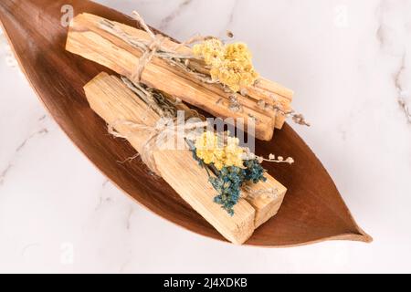 Holy wood sticks with dried flowers bouquet for meditation and spiritual  practices, wooden tray with palo santo sticks on white marble table  background, Stock image