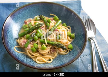 Spaghetti carbonara with green asparagus on a blue plate with napkin and cutlery, selected focus, narrow depth of field Stock Photo