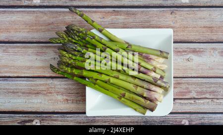 Organic green asparagus on a white plate with rustic wooden table background. Stock Photo