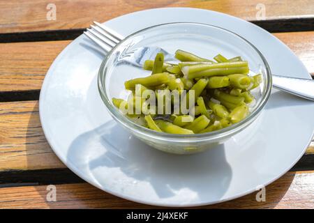Small side salad of pickled green beans with onions and herbs in a glass bowl on a white plate with a fork, selected focus, narrow depth of field Stock Photo
