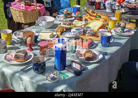 Large table set at a casual outdoor Easter brunch with family and many guests full of food in the garden on a sunny day, selected focus, narrow depth Stock Photo