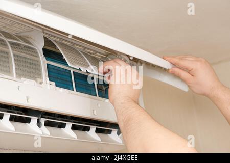 The master removes the dusty filter of the air conditioner. Maintenance and repair of air conditioners. Stock Photo