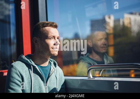 Man commuting by tram. Adult passenger looking out window of train of public transportation. Stock Photo