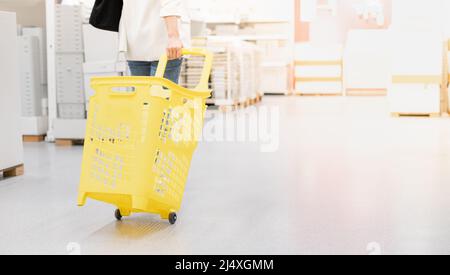 Female hand pulling the yellow plastic trolley for shopping to buy the decoration element for interior room. Stock Photo